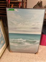 Full view of the framed seascape painting showing ocean waves, cloudy sky, and framed with protective corners.