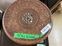 Top view of round wooden plant stand with carved floral design and central inlay