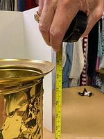 Photo showing approximate height of brass umbrella stand at about 18 inches using tape measure held by hand.