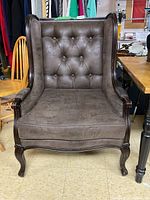 Full view of the wing chair showing brown tufted upholstery and wooden frame with carved front legs.