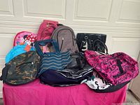 Nine assorted bags displayed on table including backpacks and tote bags, showing color and style variety.