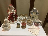 Photo showing Christmas-themed lot items arranged together including Fitz and Floyd Santa cookie jar, Lenox snowman figurine, ceramic house, reindeer tea light holder, Santa cup, ornaments, and candles