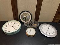 All five clocks arranged on a surface, showing size, style, and condition with visible dust and scratches.