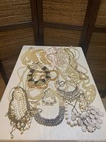 Overview photo of assorted white and cream necklaces on a flat surface with various bead sizes and styles including multi-strand, collar, and layered designs.