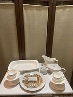 Photo showing the white ceramic roaster dish, the unmarked gravy or sauce server with lid, the white porcelain sugar bowl with lid and spoon, four white cups with saucers, and a decorative plate with Kitchen Prayer design.
