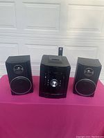 Photo of the full Sharp mini shelf speaker system including central unit and two speakers shown on pink surface.