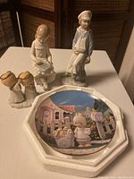 Four porcelain figurines plus a Precious Moments collectible plate shown on table.