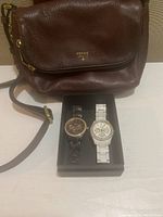 Two Fossil women's watches in a box: white tone chronograph model ES1967 and tortoise shell multifunction model ES2795, showing watch faces and bands.