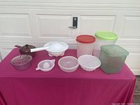 Varied plastic storage containers including large, medium, and small sizes, white plastic juicer, and two glass pots with lids arranged on table.