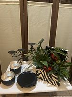 Photo showing black and white zebra-striped chest with artificial floral arrangement, black metal 5-candle holder stand, two small black vases with silver accents, and medium black candleholder on a white surface.