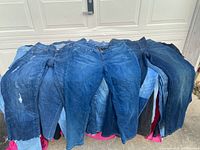 Pile of assorted ladies jeans in different shades of blue and black, showing full length of multiple pairs.