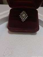 Front view of the cluster ring with clear stones arranged in a diamond pattern inside a velvet ring box.