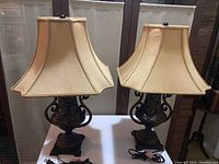 Pair of two table lamps with beige hexagonal fabric shades and decorative dark bases shown together on white surface.