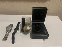 Four men's watches displayed on table including ESQ by Movado dress watch, Timex wristwatch, vintage Dad quartz pocket watch and Sean John pocket watch in box