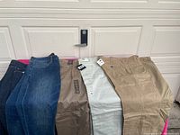 Pants laid out front view includes 2 jeans and 3 khaki pants on pink cloth