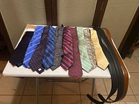 10 men's neckties of various colors and designs alongside 3 black leather belts on a small table.