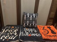Pillow covers and stuffed pillow displayed flat and stacked, showing skeleton design pillow on top and various Halloween text and themed covers beneath