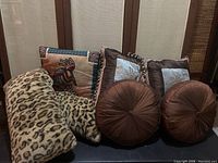 Group photo showing all pillows including 2 leopard fuzzy bolsters, 2 southwestern motif square pillows, 2 round brown pillows with button tufting, and 1 smaller southwestern square pillow.