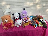 Multiple assorted plush animals including teddy bears, a panda, a unicorn backpack, and smaller animals shown together for overview of lot contents.