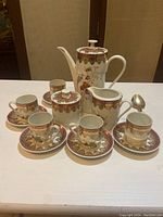 All items of the coffee set arranged on a white surface showing the coffee pot, cups, saucers, creamer, and sugar cup with lid.