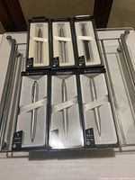 Full view of the six Sheaffer pens in original packaging arranged in two rows on a glass surface.