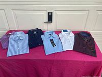Six folded men's dress and casual shirts laid on a table, showing variety of colors and patterns.