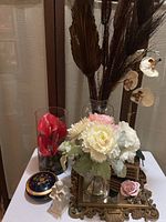 Table with various floral arrangements, porcelain bowl, angel figurine, mirror, and pink rose figurine on top
