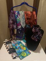 Scarfs hanging on a blue hanger showing a variety of printed designs and colors; folded scarfs displayed on the table; one scarf styled on a black mannequin bust.