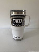 Front view of the white 20 oz Yeti Rambler travel mug with handle and its label.