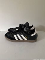 Side view of Adidas Samba sneakers showing black leather shoes with white stripes, gum sole, and gold Samba text.