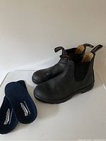 Pair of black leather Blundstone boots with new blue insoles placed beside them on a white surface