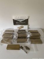 19 brass finish rectangular finger pulls sealed in plastic with screws in front and package in background.
