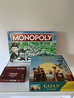 Photo of Monopoly, Catan Junior, and Exploding Kittens games boxes stacked showing front of each box.