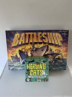 Photo showing two board games: Battleship and Herding Cats in their original boxes.