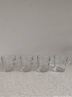Four clear glass espresso mugs placed on a kitchen countertop, showing their size and shape.