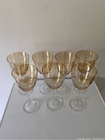 Front-facing view of seven peach lustre stemmed wine glasses arranged in two rows showing clear stems and softly colored bowls.