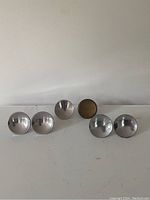 Set of six mid century modern round concave knobs on a white surface, five with chrome finish and one with brass finish.