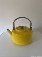 Front and side view displaying the bright yellow enamel body, teak handle, and lid knob of the kettle.