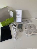Photo of Auvon TENS machine with accessories including user manual, electrode pads, cables, carrying pouch, and packaging box on a white surface.