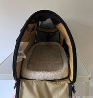 Front view of black Bergan soft pet carrier showing structured interior base with rimmed beige fleece bed insert.