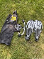 Two sets of Body Glove snorkeling equipment laid on grass, featuring masks, snorkels, fins in two size categories, and mesh carrying bags with brand logo.