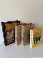 Photo showing all four books in the lot standing side by side: Last of the Mohicans hardcover, Shakespeare complete works volumes 1 and 2 hardcovers, and The Three Musketeers paperback.