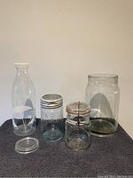 Full view of all five vintage glass containers including bottles, jars, and crocks arranged on a flat surface.