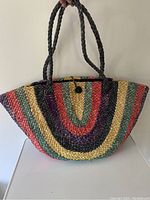 Front view of vintage woven straw tote showing colorful vertical stripes and braided black handles.