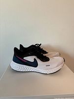 Side profile of left shoe showing white mesh, black lace area, navy blue and purple Nike branding, white cushioned sole.