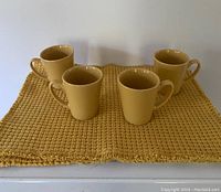 Four yellow ceramic mugs arranged on one of the yellow woven placemats.
