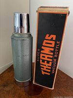Photo of vintage green textured metal vacuum bottle with chrome cup lid alongside original black and orange box.