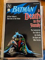 Batman comic titled 'A Death in the Family' featuring Batman holding Robin, dark cover with blue and red text.