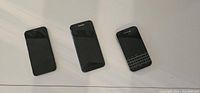 Front view of three smartphones: BlackBerry Classic on right, Samsung in middle, iPhone on left all face up on white surface to show physical details.
