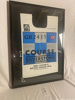 Framed yellow flag marshal tabard from 2001 British Grand Prix, showing full front view at an angle.